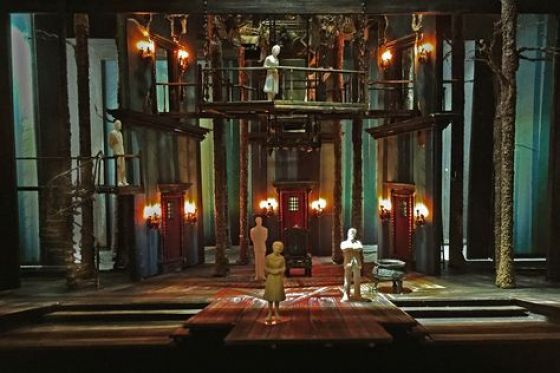 A theatrical set design features a multi-level stage with wooden structures